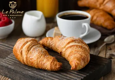two croissants and a cup of coffee on a wooden table at Le Palme in Terrasini