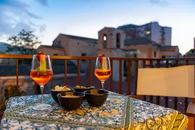 a table with two wine glasses and snacks on a balcony at La Paperella Blu Apartment in Termini Imerese