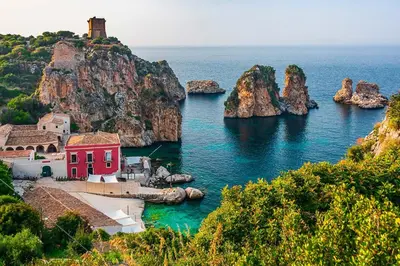 a red house in the water next to a group of rocks at Carducci Loft in Castellammare del Golfo