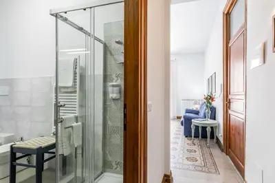 a glass shower in a bathroom with a blue chair at GuestHost - Terry's Garden in Palermo in Palermo