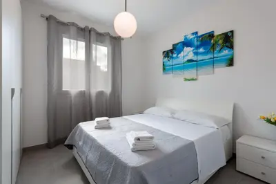 a white bedroom with a bed and a large window at Savoia's apartments in San Vito lo Capo