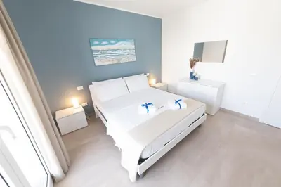 a white bedroom with a white bed and blue walls at Alta Marea Sea Apartments in Balestrate