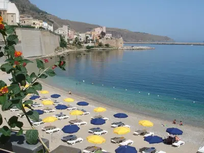 a beach with blue and yellow umbrellas and the ocean at Hotel Al Madarig in Castellammare del Golfo