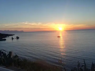 a sunset on the water with a boat in the water at Terra Sinus Luxury apartment in Terrasini