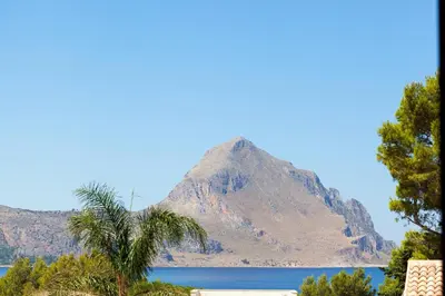 a mountain with a palm tree in front of a lake at LA DAMA in San Vito lo Capo