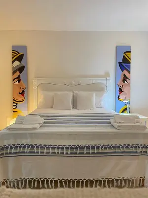 a bedroom with a large white bed with paintings on the walls at Surfinia’s home in Palermo