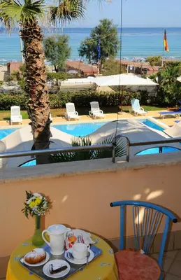 a table with a tray of breakfast food on a balcony with a pool at Hotel Sirenetta in Isola delle Femmine