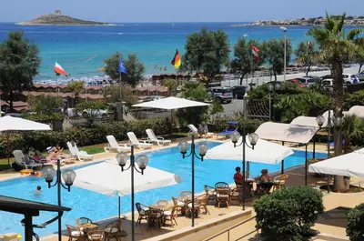 a pool with white umbrellas and chairs and the ocean at Hotel Sirenetta in Isola delle Femmine