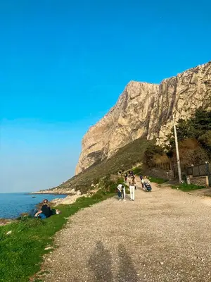 a group of people walking on a gravel road near the ocean at Itaca in Palermo