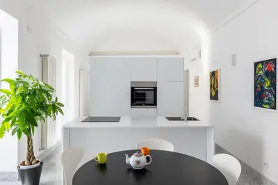 a white kitchen with a black table and chairs at Suite Bellini 5 Apartment in Palermo