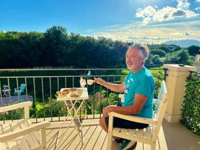 a man sitting in a chair on a balcony with a plate of food at Esmaraldas House of Love in Terrasini