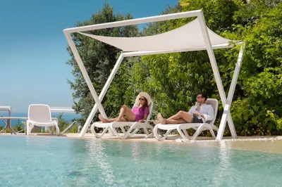 a couple sitting on chairs next to a swimming pool at Hotel La Tavernetta in Scopello