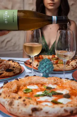 a woman is pouring a glass of wine over a table with pizzas at Agriturismo Villa Cefalà in Santa Flavia