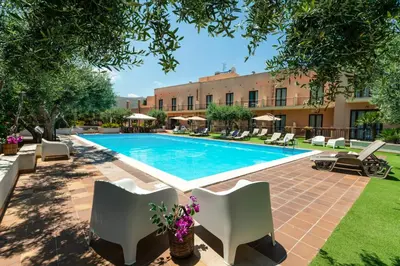 a swimming pool in a courtyard with chairs and a building at Hotel Achibea in San Vito lo Capo