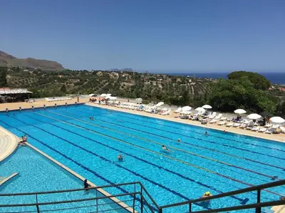 a large swimming pool with people in it next to a beach at Allegroitalia Torre Artale Palermo in Trabia