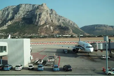 an airplane parked at an airport with a mountain in the background at Sicilia Nica - appartamento privato a Cinisi (PA) in Cinisi