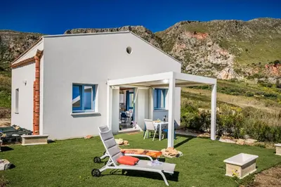 a white house with a lawn with a chair at Villa Holidays in Torre Bennistra in Scopello