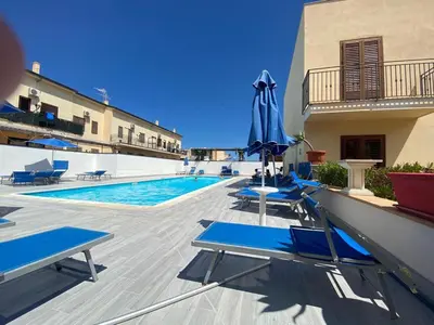 a swimming pool with blue lounge chairs and an umbrella at Coral sea B2 in San Vito lo Capo