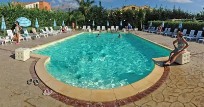 a swimming pool with a woman sitting on a chair in it at Villa indipendente le coccinelle beach mare piscina a 250 mt dal mare con servizio di piscina a 400 mt 12 k da Cefalu in Campofelice di Roccella