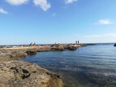 a group of people sitting on the rocks at the beach at Holiday & House - Imparato Carini Costa Verde - Appartamento con giardino privato - porzione di Villa residenziale a pochi passi dal mare in Carini