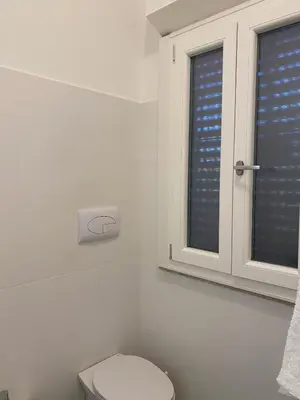 a white bathroom with a toilet and a window at Holiday & House - Imparato Carini Costa Verde - Appartamento con giardino privato - porzione di Villa residenziale a pochi passi dal mare in Carini