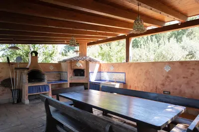 an outdoor dining area with a wooden table and an oven at Villa Premiere immersa nel verde a Castelluzzo in Castelluzzo