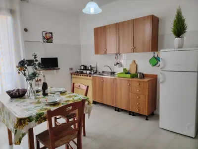 a kitchen with a table and a white refrigerator at Casa Derna 25dx Climatizzata in Castellammare del Golfo