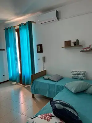 a room with two beds and blue curtains at Casa Conturrana,10 metri dalla spiaggia di San Vito in San Vito lo Capo