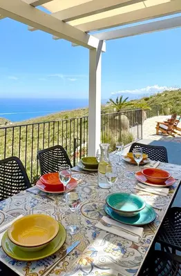 a table with plates and wine glasses on a patio at Villa Felice - SEAVIEWS & PRIVATE POOL in Scopello