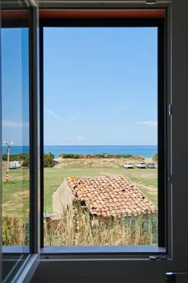 a window with a view of a field and the ocean at Salinelle Rooms in Lascari