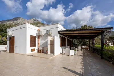 a white house with a roof with mountains in the background at Pittalumari Makari in Macari