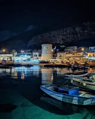 a group of boats sitting in the water at night at mansarda beach Mondello in Palermo