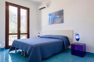 a white bedroom with a blue bed and a window at Casa Orchidea Bianca in San Vito lo Capo
