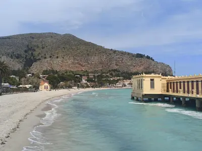 a beach with a building on the water and a mountain at Mondello Blue Sea in Mondello